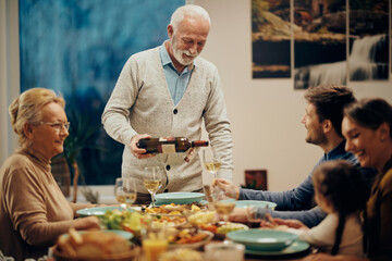 Happy mature man serving wine during family lunch in dining room.
