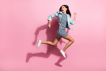Full length photo of charming frightened lady wear striped dress jumping running fast looking back isolated pink color background