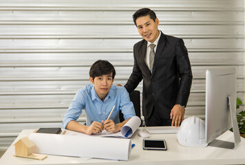 Asian senior good-looking boss in suit sitting at desk and working with junior employee in office...