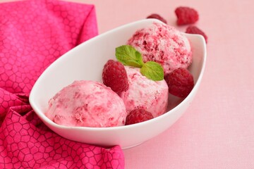 Scoops of raspberry ice cream in a bowl garnish with mint leaves. Summer dessert