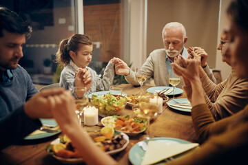 Grateful multi-generation family saying grace at dining table.