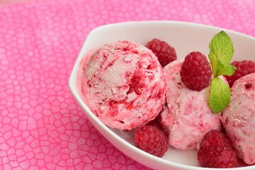 Scoops of raspberry ice cream in a bowl garnish with mint leaves. Summer dessert