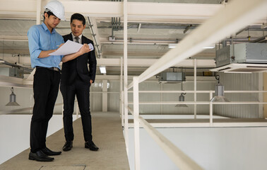 Asian businessman boss wearing black suit standing and discussing with young engineer in construction site. Concept for brainstorming, review, and inspecting work results