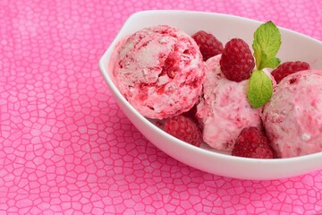 Scoops of raspberry ice cream in a bowl garnish with mint leaves. Summer dessert