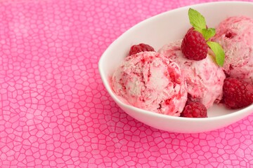 Scoops of raspberry ice cream in a bowl garnish with mint leaves. Summer dessert