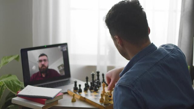 A young cute man plays chess on a video call at a house during a corona pandemic