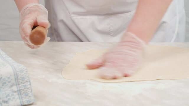 The cook rolls out thin dough with a wooden dough roller on the table with flour.
