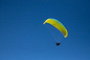 gelber gleitschirm unter blauem Himmel, Pilot in Wärmesack im Gleitflug bei sonnigem Frühling nahe 