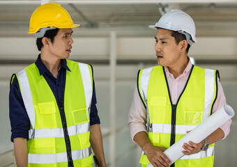 Portrait of young and handsome two Asian male engineers in yellow protective vest working and taking with intimated gesture in factory