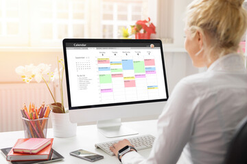 Woman using calendar on computer to organize her schedule at work - obrazy, fototapety, plakaty