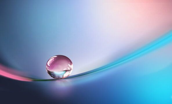 Beautiful clean transparent bright drop of water on smooth surface in blue and pink colors, macro. Creative image of beauty of environment and nature.