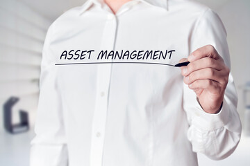Businessman hand holds a pen and underlines the words asset management on virtual screen. Managing...