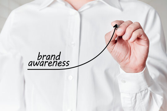 Businessman with pen draws a rising line graph with the word brand awareness on a virtual screen. Increasing brand awareness