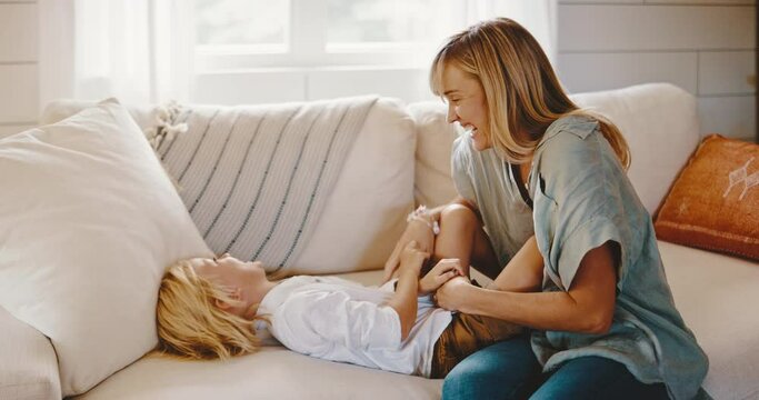 Mother and cute young kid playing on the couch, laughing and tickling, family lifestyle at home