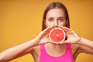 Beauty portrait of a lovely young woman with long hair standing over yellow background, showing slices of a grapefruit.