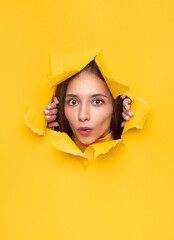 Astonished woman peeking from hole in paper