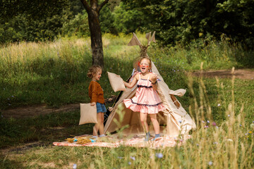 Two funny girls are playing next to wigwam in summer in the countryside. © Natalia
