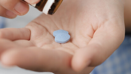 Two big blue diamond-shaped pills labeled 100 fall into palm of hand from pill bottle. Close-up,...