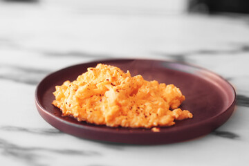 Creamy omelet, scrambled eggs on a purple plate on a marble background