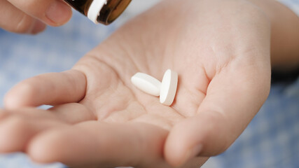 Two big white pills oval diamond-shaped elongated shapes fall into palm of hand from pill bottle....