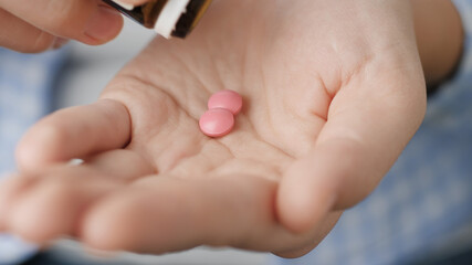 Two big pink round shapes fall into palm of hand from pill bottle. Close-up, front view, center composition