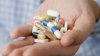 Handful of tablets and capsules of various shapes and colors lie in palm of your hand. Close-up, front view, center composition