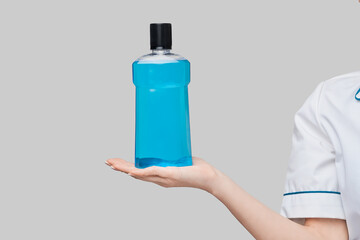woman dentist doctor holding bottle of mouthwash standing over grey background