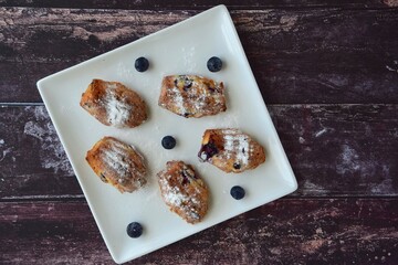 Blueberry Madeleine cookies on a plate with dark wooden background. Flat lay
