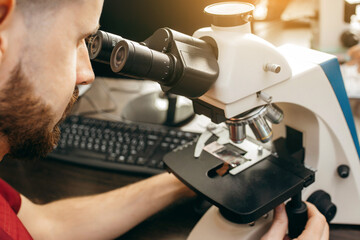 A doctor sits in a laboratory and makes a study under a microscope