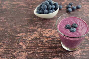 Fresh blueberry smoothie in a glass on wooden background. Negative space