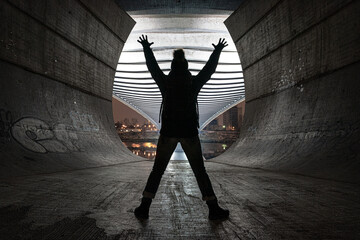 Woman with a knitted hat standing in under the bridge structure with in the backlight. Success...
