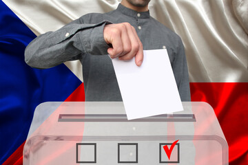 male voter lowers the ballot in a transparent ballot box against the background of the national...
