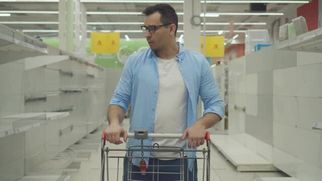 a confused and puzzled male customer in a store against the background of empty shelves