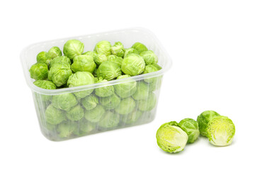 Organic brussels sprouts in disposable plastic container and outside it isolated on white background.	