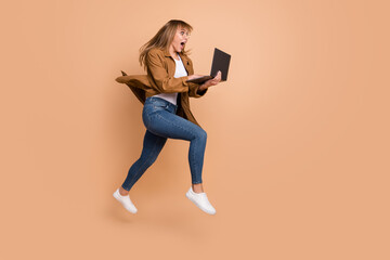 Full body profile side photo of nice amazed blonde woman hold computer jump up run empty space isolated on beige color background