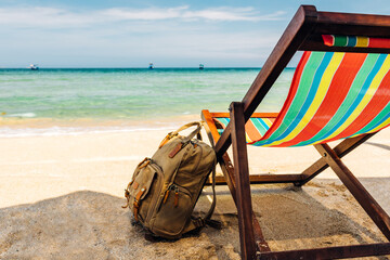 open sea, A deck chair on the sandy shore of a tropical beach. stylish brown backpack standing nearby. traveler, freelancer