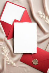 Fototapeta premium Luxury wedding invitation card mockup and envelopes on beige silk. Flat lay, top view, copy space. Elegant wedding stationery set.