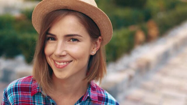 Close up portrait of young tourist girl in hat with beautiful eyes sitting on street and looking at camera smiling.