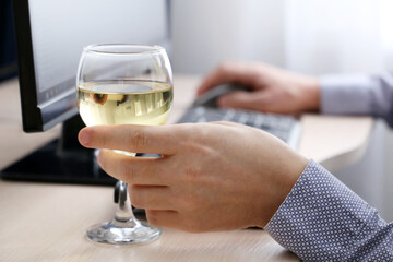 Glass of white wine in male hand, man drinking alcohol sitting at PC keyboard. Remote work at home or relax at office
