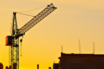 Silhouette of a crane on a background of sunset. Ropes and hooks on an orange background.