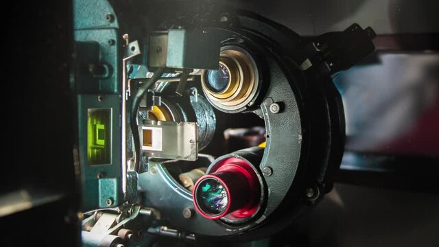 Cinema projector industrial 35mm machinery working in projectionist booth, moving images defocused in audience screen in background