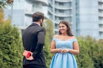 Man hiding gift behind back and smiling woman