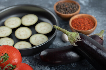 Sliced raw eggplants in frying pan with tomato and spices