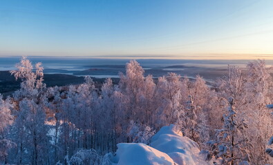 Winter landscape with snow-covered forest, mountains, sky, frosty haze in the rays of the setting sun