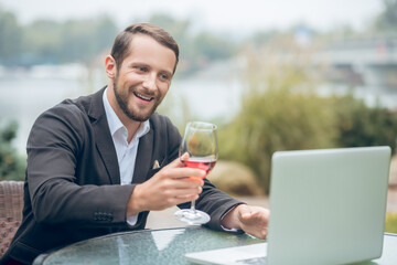Man with wineglass communicating online at laptop