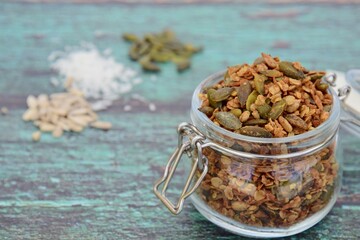 Homemade granola in a jar, made from gluten free oats, pumpkin seeds, sunflower seeds, coconut flakes, maple syrup and coconut oil. Green wooden background
