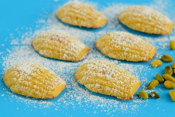 Pistachios Madeleine with powdered sugar on blue background.