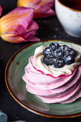 Pavlova cake with blueberries on a plate close-up, tea and pink tulips vertical photo