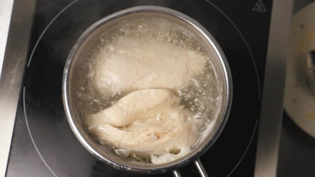 View of chicken breasts are boiling in a metal saucepan at kitchen restaurant. Chicken fillet is cooking in stewpan at cuisine. Concept of preparing meat. Top view Slow motion