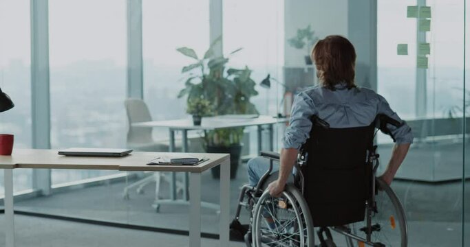 Disabled man working in corporate office coming to desk opening laptop communicating doing work online. Business person. People with disabilities.